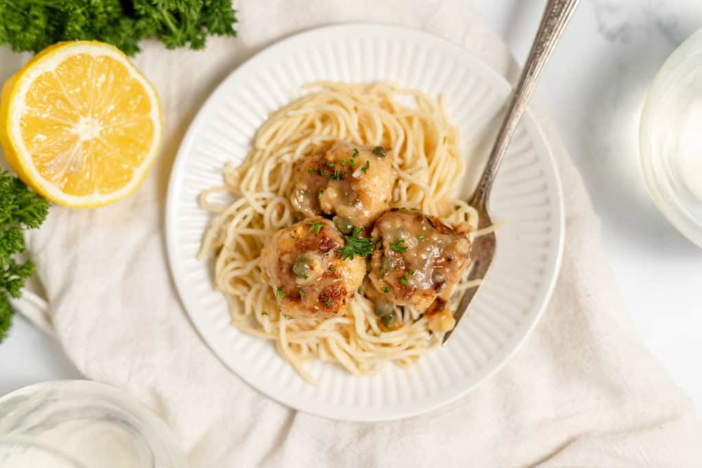 A plate of spaghetti with shrimp, garnished with chopped herbs and paired with a half lemon and parsley on the side.