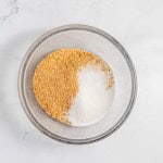 A glass bowl containing equal parts of brown and white granulated sugars rests on a marble surface, ready to sweeten your perfect lemonade pie.