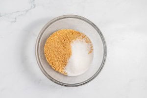 A glass bowl containing equal parts of brown and white granulated sugars rests on a marble surface, ready to sweeten your perfect lemonade pie.