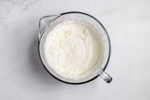 A glass bowl filled with creamy, whipped lemonade pie mixture rests on a white marble surface.