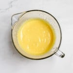 A glass measuring cup filled with a yellow, creamy lemonade pie mixture rests on a white marble surface.