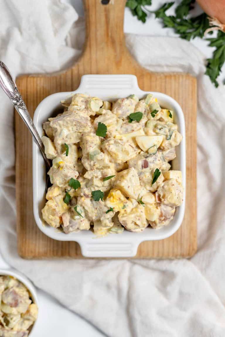 A close-up of mustard potato salad in a white dish, garnished with fresh herbs.