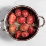 Top view of red potatoes in a stainless steel pot on a marble countertop, ready for making mustard potato salad.