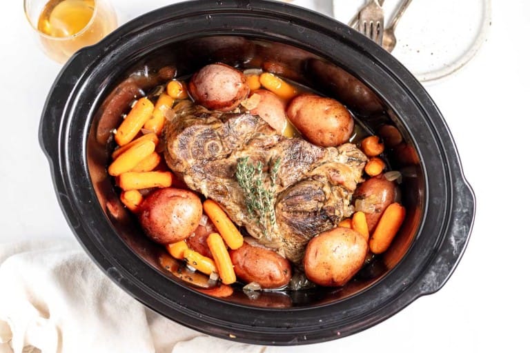 A pot roast with carrots and potatoes in a slow cooker, viewed from above.