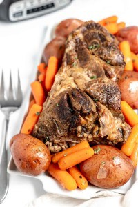 A plate of braised lamb shanks with carrots and potatoes, seasoned with herbs, ready to serve.