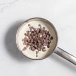 A small saucepan containing a creamy liquid and chocolate chips on a marble surface.