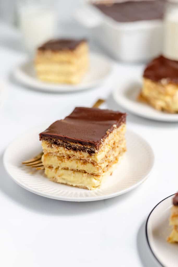 Slices of layered dessert topped with chocolate glaze on white plates.