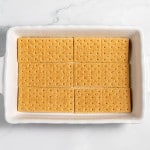 A rectangular white baking dish contains two rows of four graham crackers neatly arranged on the bottom surface.