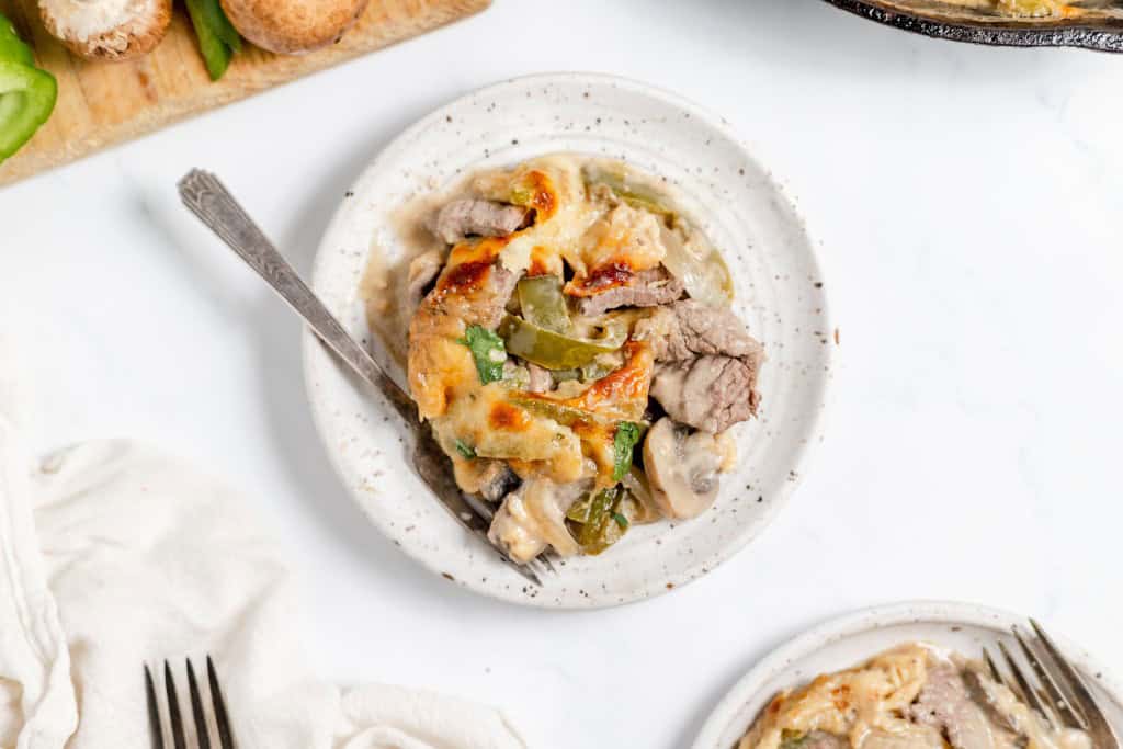 A plate of a baked dish featuring meat, green peppers, and mushrooms in a creamy sauce, with a fork rested on the side.