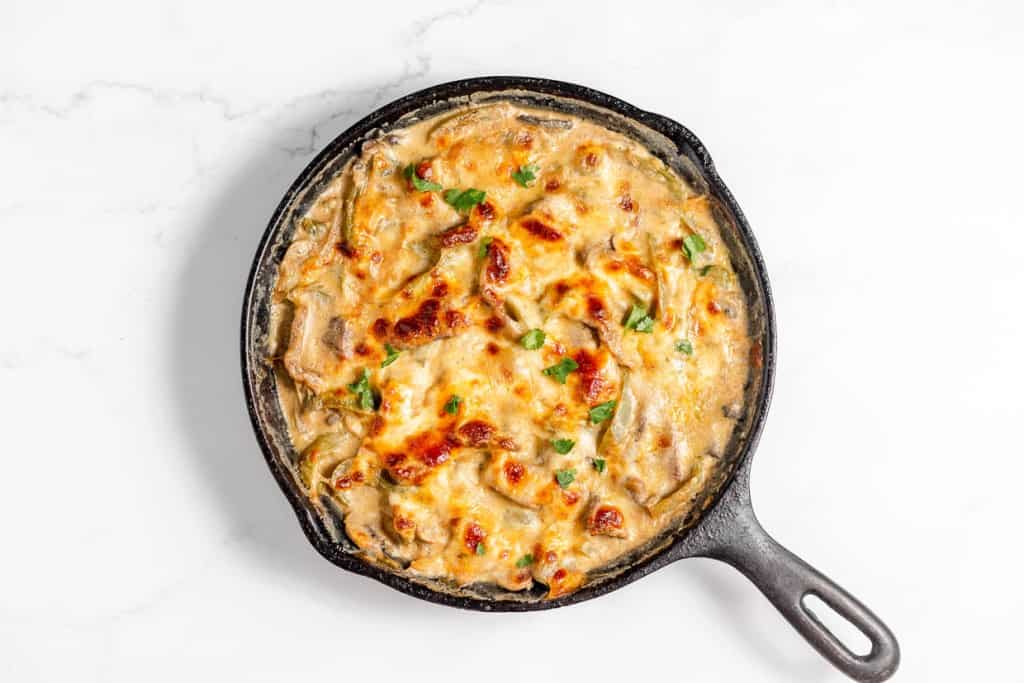 An overhead view of a cast iron skillet filled with a baked cheesy Philly Cheesesteak Casserole dish topped with chopped herbs, resting on a white marble surface.