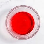 A clear bowl containing a bright red liquid, placed on a white marble surface.