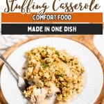 A serving of Chicken and Stuffing Casserole sits on a white plate with a fork, placed on a wooden surface.