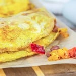 Close-up of an omelet filled with diced ham and bell peppers placed on parchment paper, with eggs and a partially visible plate in the background—perfect for your breakfast ideas.