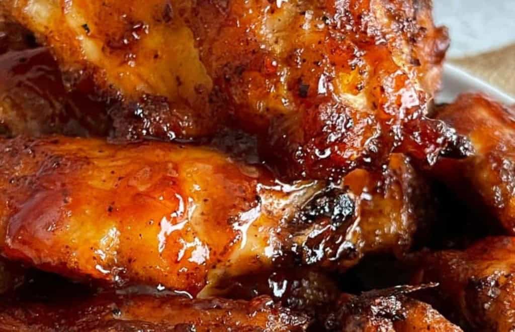 Close-up of a heap of glazed, grilled chicken wings with crispy, caramelized skin, showcasing their golden-brown color and texture.