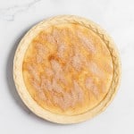 An unbaked pie with a crimped edge crust, filled with a mixture and topped with a sprinkled layer of cinnamon and sugar, on a marbled white surface.