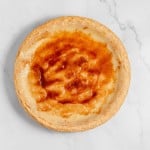 A baked custard pie with a light golden brown top and a flaky crust is placed on a white marble surface.