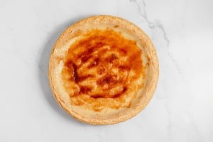 A baked custard pie with a light golden brown top and a flaky crust is placed on a white marble surface.
