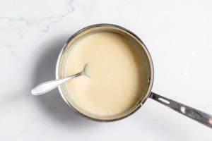 A pot of creamy white sauce with a spoon resting in it on a marble countertop.