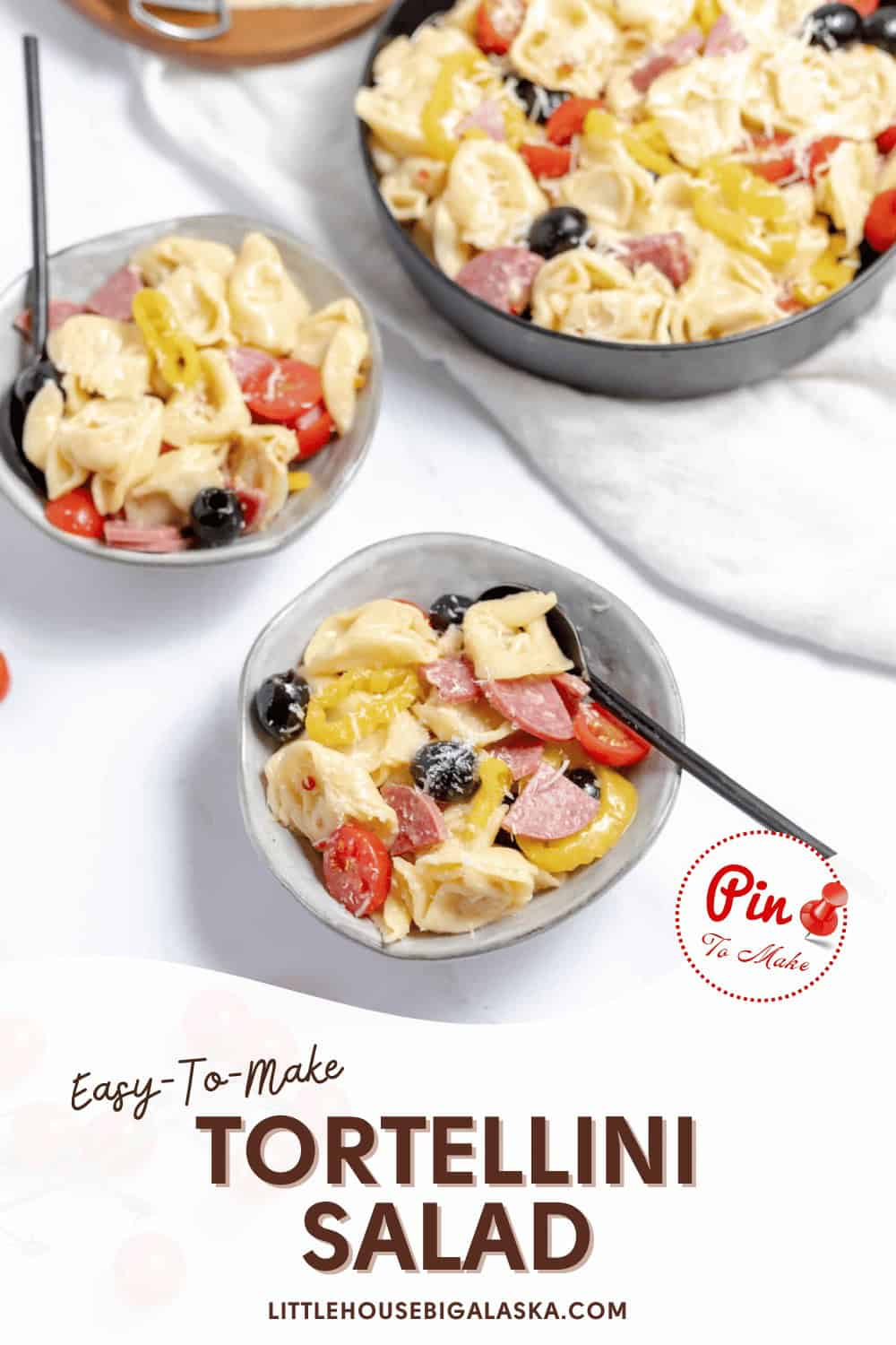 Bowls of tortellini salad with olives, tomatoes, and salami slices are shown with a large serving dish in the background. Text overlay reads "Easy-To-Make Tortellini Salad" and "LITTLEHOUSEBIGALASKA.COM".