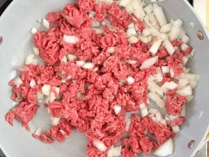 A pan with ground beef and chopped onions being cooked for a delicious Unstuffed Zucchini Casserole.