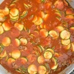 A pan filled with tomato-based sauce, zucchini slices, and ground meat sizzles on the stovetop, creating a delightful Unstuffed Zucchini Casserole.