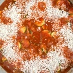 A skillet filled with white rice, tomato sauce, and sliced zucchini being prepared on a stovetop resembles an unstuffed zucchini casserole in the making.
