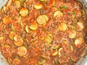 A close-up of a skillet filled with Unstuffed Zucchini Casserole, featuring a hearty mix of sliced zucchini, ground beef, rice, diced tomatoes, and rich sauce.