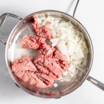 Ground beef and chopped onions cooking in a stainless steel pan on a stovetop.