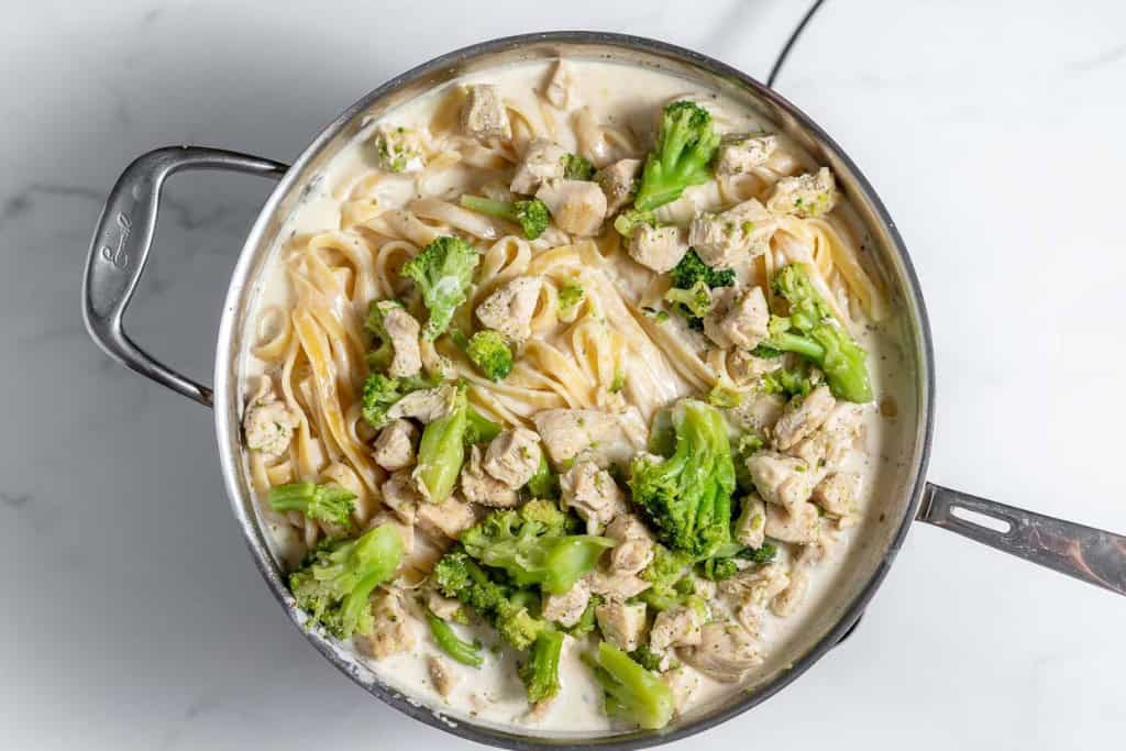 A pot filled with creamy pasta, chunks of chicken, and broccoli florets.