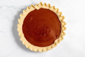 A raw pie with crimped edges filled with chocolate filling, ready to be baked.