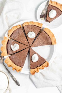 A sliced chocolate pie with whipped cream on each piece, displayed on a white plate with one slice served on a separate small white plate.