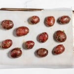 A baking sheet with parchment paper holds twelve seasoned small red potatoes, ready for roasting.