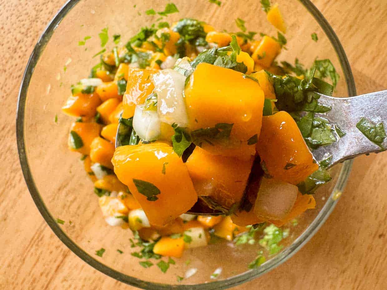 A bowl of mango pico de gallo with diced mango, onion, cilantro, and lime.