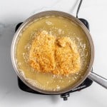 Two breaded cutlets frying in a pot of oil on a stovetop.