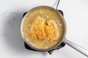 Two breaded cutlets frying in a pot of oil on a stovetop.