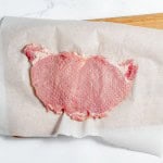 Raw pork chop placed on parchment paper atop a wooden cutting board.