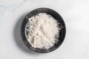 A black bowl filled with white flour sits on a white marble surface.