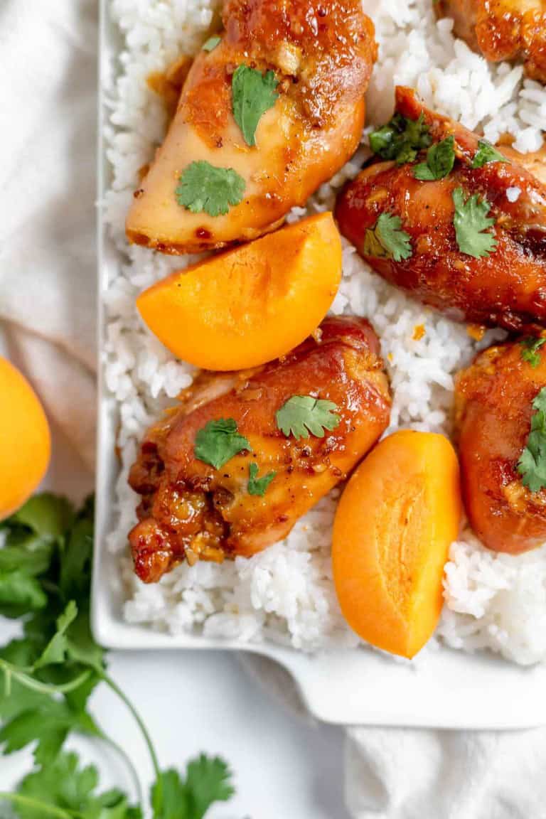 A dish featuring cooked chicken pieces garnished with cilantro, served over white rice, accompanied by slices of orange fruit.