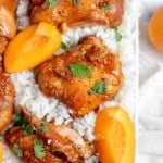 Close-up of roasted chicken pieces garnished with cilantro, placed on a bed of white rice with fresh apricot slices.