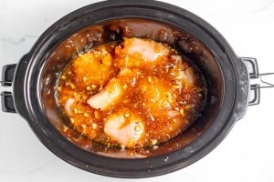 Chicken breasts marinating in a slow cooker with a mix of diced vegetables, spices, and sauce.
