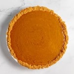 A top view of a pumpkin pie with a graham cracker crust on a white marble surface.
