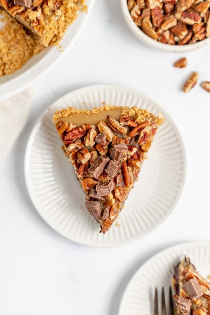 A slice of pie topped with chopped pecans and chocolate pieces on a white plate.