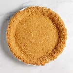 A plain, homemade graham cracker pie crust in a white pie dish on a marble countertop.