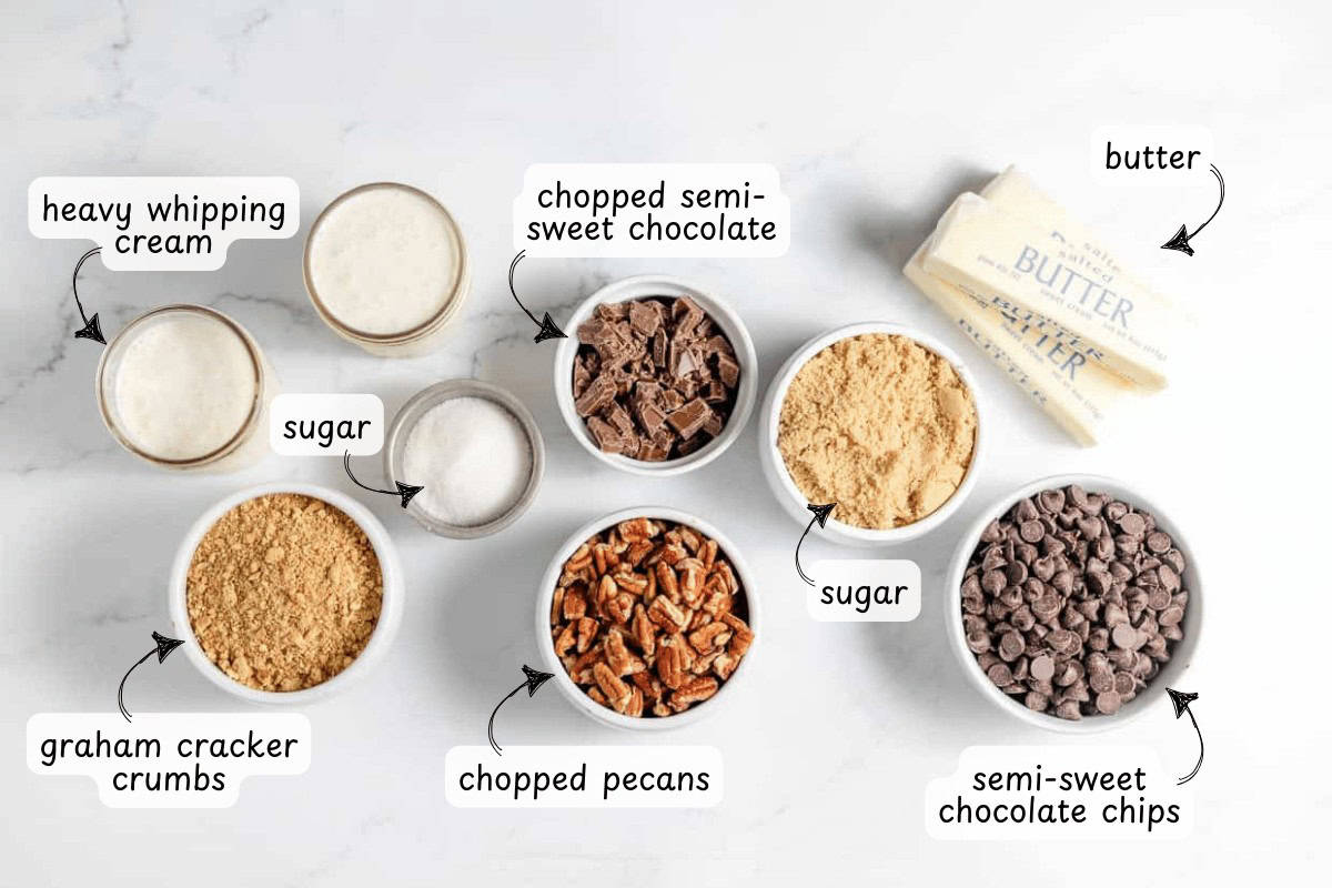Ingredients on a white surface: heavy whipping cream, sugar, chopped semi-sweet chocolate, semi-sweet chocolate chips, butter, graham cracker crumbs, chopped pecans—perfect for making a decadent turtle pie.