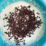 A blue mixing bowl filled with cookie dough and topped with chocolate chips.