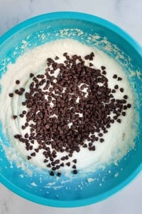 A blue mixing bowl filled with cookie dough and topped with chocolate chips.