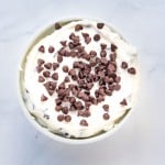 A bowl of white creamy dip topped with chocolate chips on a white marble surface.