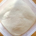 A risen dough in a square plastic container on a wooden surface.