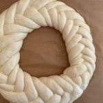 A circular braided dough ring sits on a sheet of parchment paper, ready for baking.