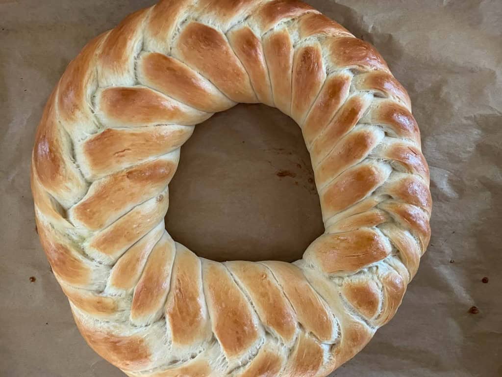 A round, braided loaf of bread with a golden-brown crust on a parchment-lined surface.